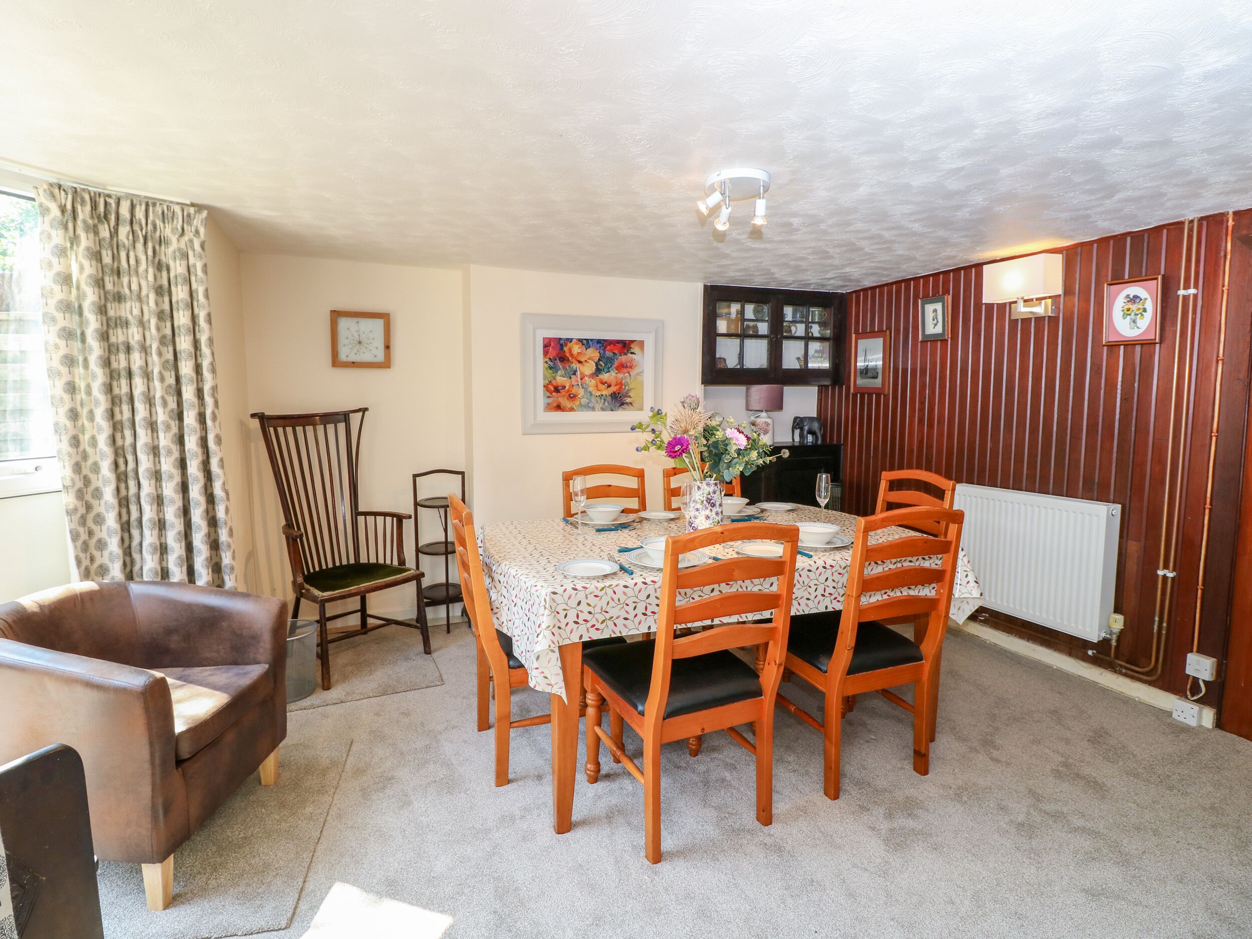 A dining area with a table set for four, surrounded by wooden chairs, a brown leather sofa, and a wooden chair with a cushioned seat.