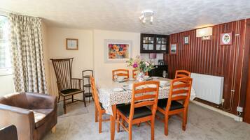 A dining area with a table set for four, surrounded by wooden chairs, a brown leather sofa, and a wooden chair with a cushioned seat.