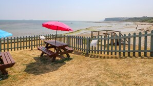 A beachside patio with picnic tables and a red umbrella, overlooking the sea. - St. Michaels House (Ryde)