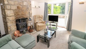 A living room with a stone fireplace, a comfortable armchair, a sofa, and a glass coffee table. - St. Michaels House (Ryde)