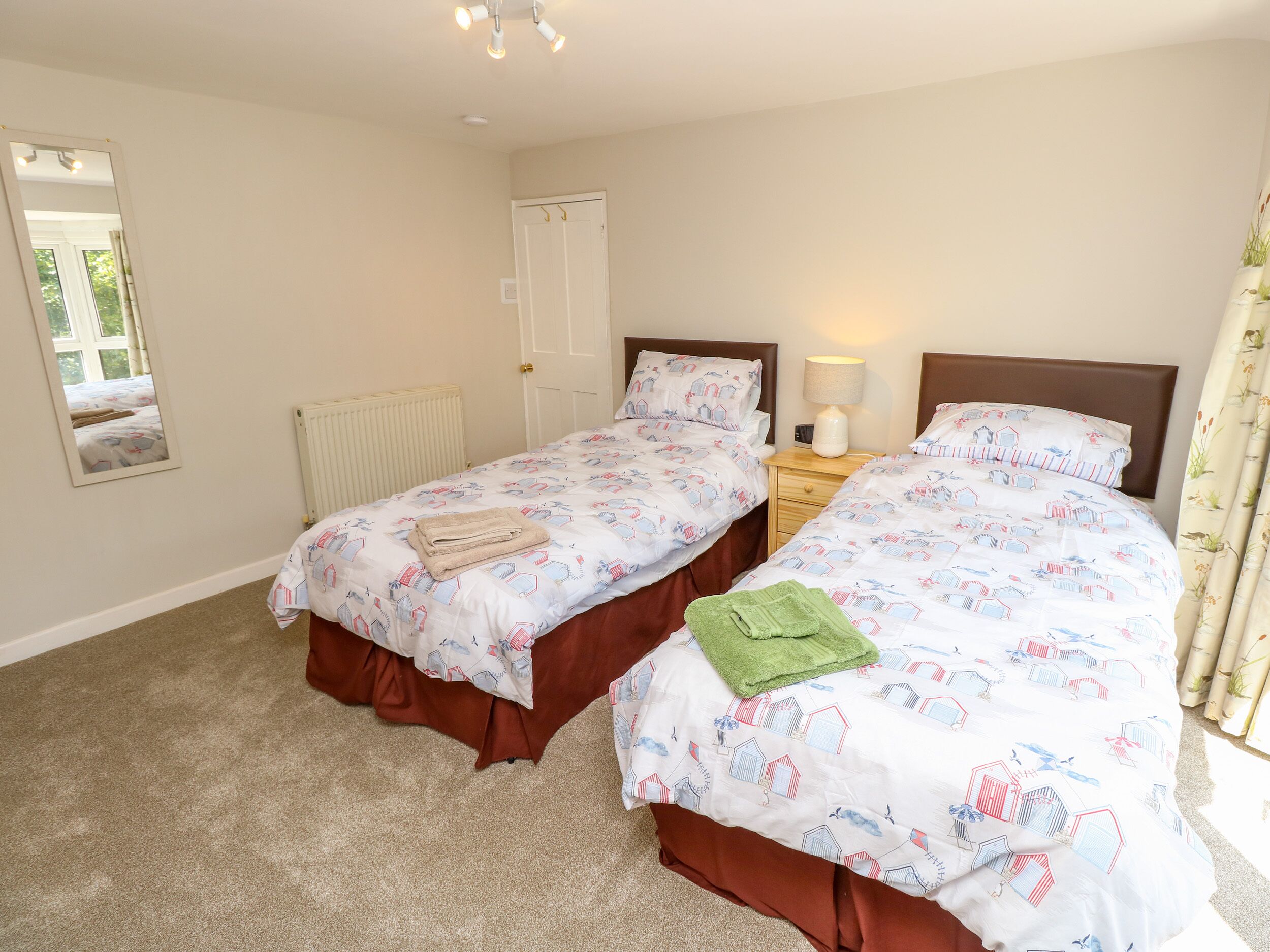 A bedroom with two beds, a radiator, a nightstand with a lamp, and a mirror.
