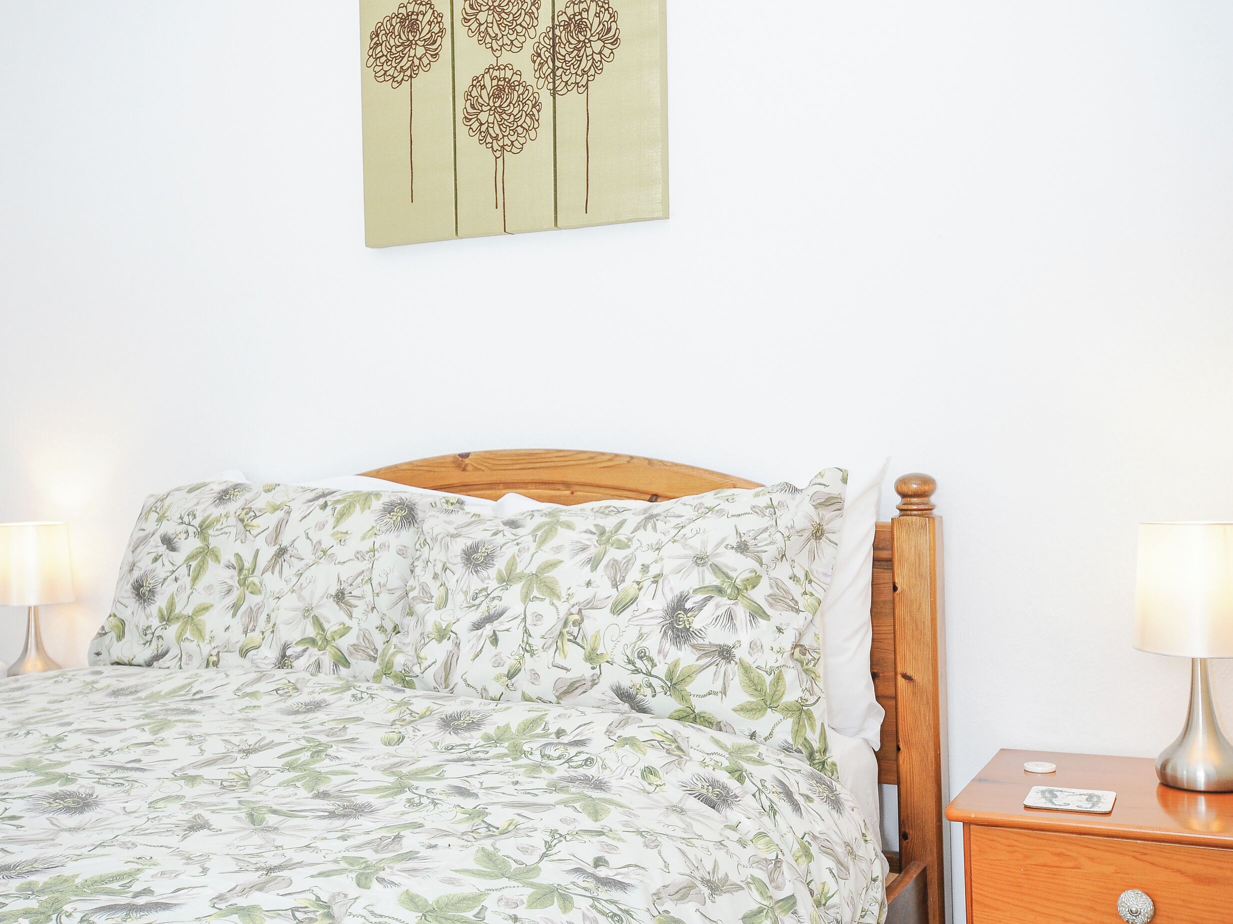 Una cama con ropa de cama floral, cabecera de madera y dos lámparas de noche.