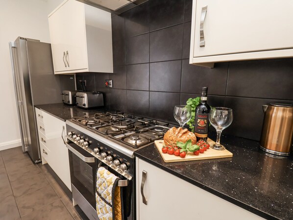 A modern kitchen with a gas stove, oven, white cabinets, black tiled backsplash, and a countertop with a bottle of Chianti, glasses, and a loaf of bread.