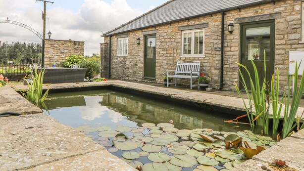 A stone cottage with a small pond, a bench, and a sign reading "Cottage." - The Cottage (Thirsk)