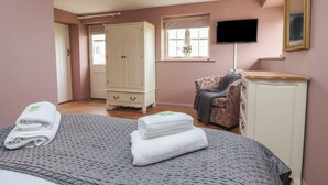 A bedroom with a bed, a wardrobe, a chair, a television, and a window. - The Cottage (Thirsk)