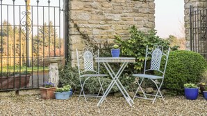 A stone wall with a metal gate, a table with chairs, and potted plants. - The Cottage (Thirsk)