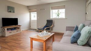 A living room with a television, a wooden coffee table, a grey sofa, and a blue armchair. - The Cottage (Thirsk)