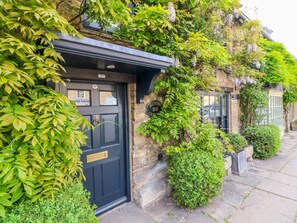 A stone building with a black door, surrounded by lush greenery and a stone pathway.