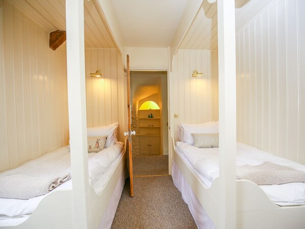 A narrow hallway with two single beds on either side, a wooden door, and a small alcove with a lamp.