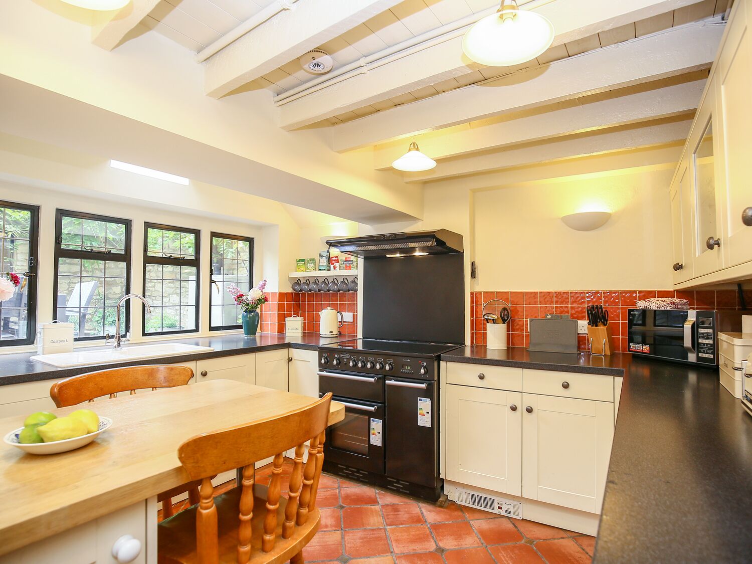 A kitchen with a central island, a stove, oven, and microwave. There are cabinets, a sink, and a window with a view of the outdoors.