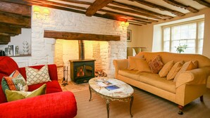 Un salon chaleureux avec une cheminée en pierre, des poutres apparentes, un fauteuil rouge, un canapé beige et une petite table.