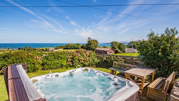 Un jacuzzi con vista al mar, rodeado de follaje y una terraza de madera.