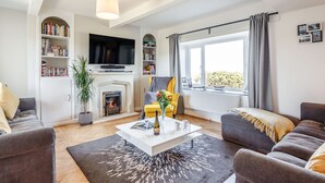 Una sala de estar moderna con chimenea, televisor de pantalla plana, estantería y un ventanal con cortinas.