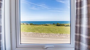 Una ventana con vista a un paisaje costero, que incluye una carretera, campos verdes y el mar.