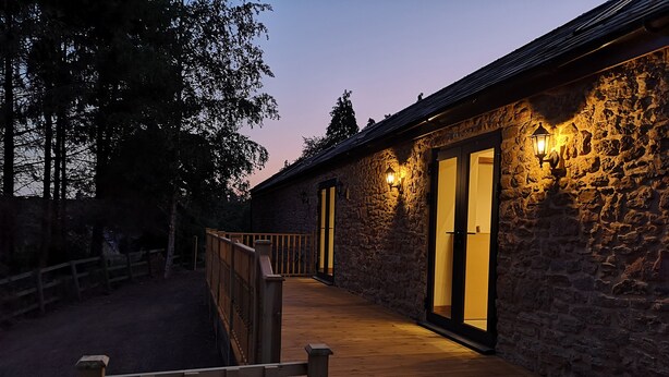 A stone building with a wooden deck and a staircase leading to a door. - The Milking Barn (Yeovil)