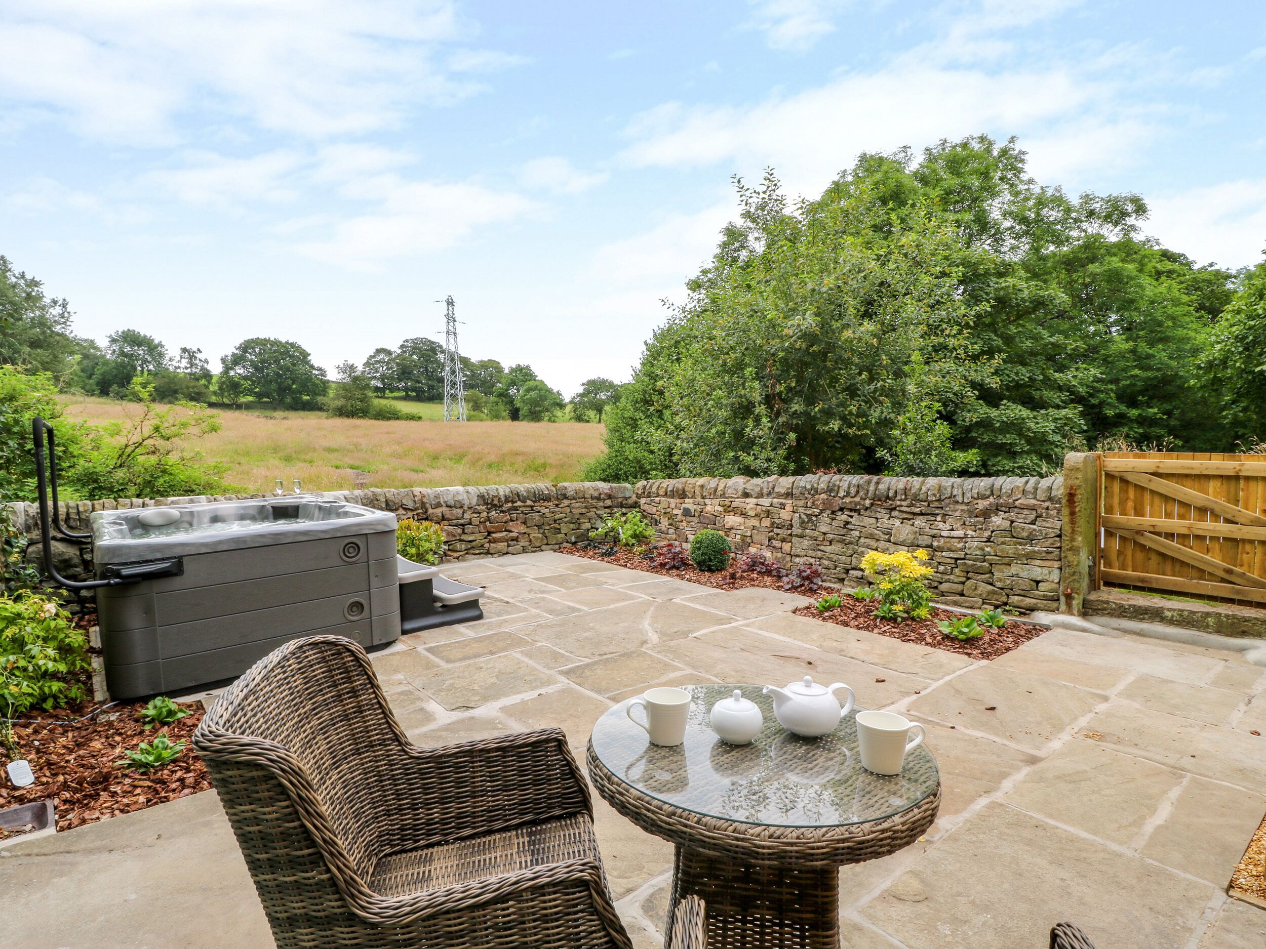 A patio area with a hot tub, wicker furniture, and a table with teapots.