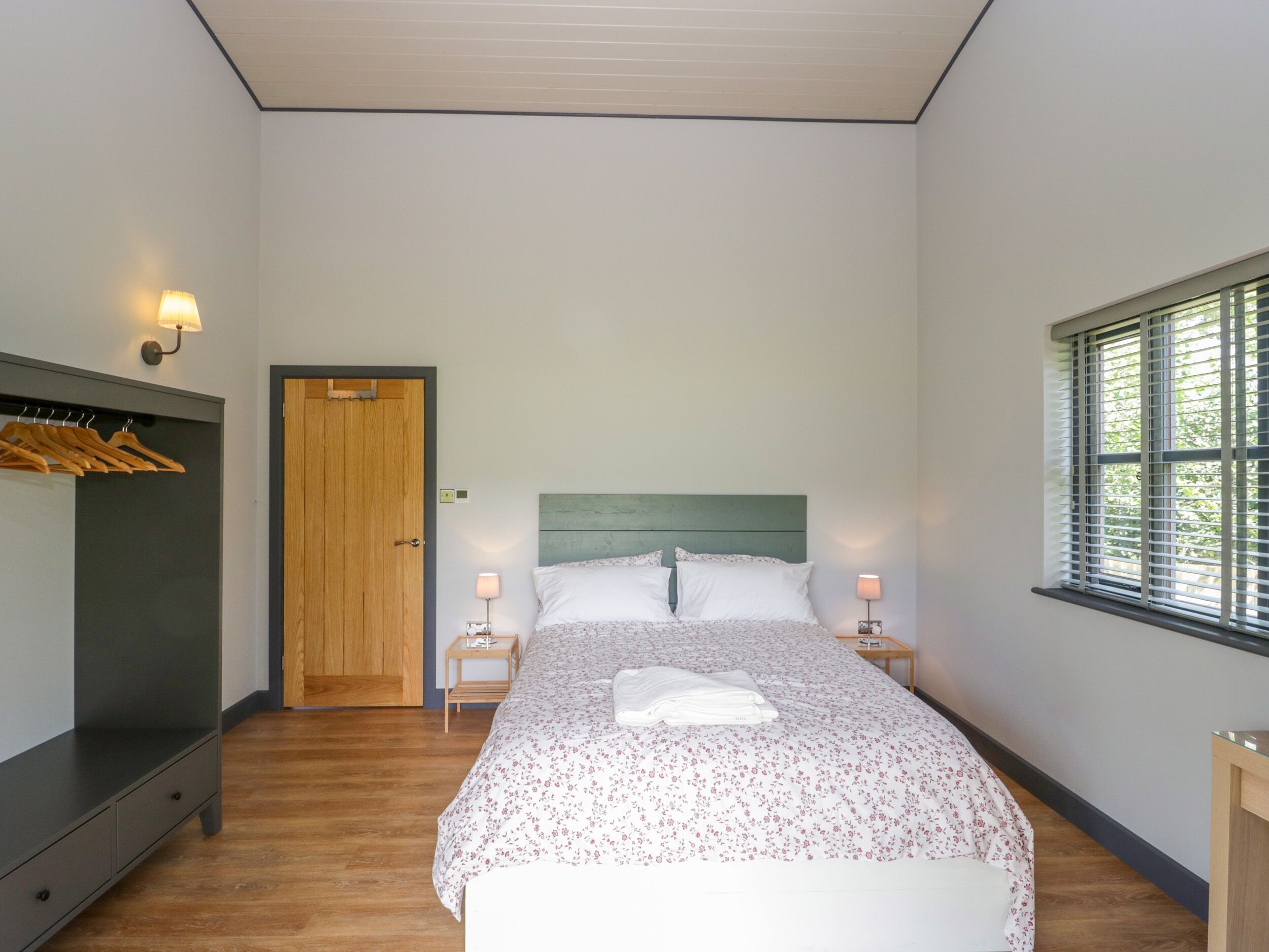 Un dormitorio con cama, mesitas de noche, un armario, una puerta y una ventana.