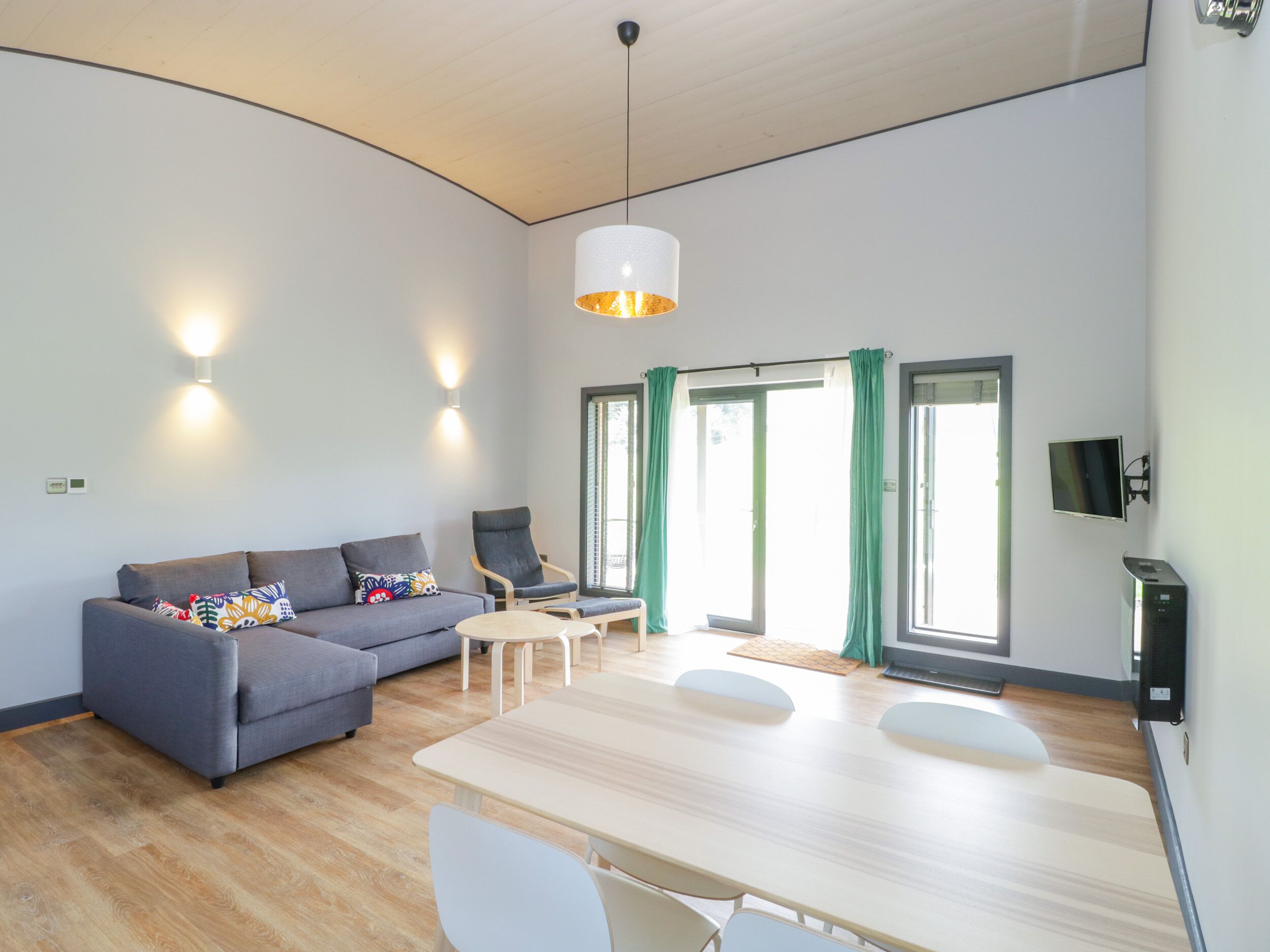 A modern living room with a grey sofa, a wooden dining table, and a hanging light fixture.