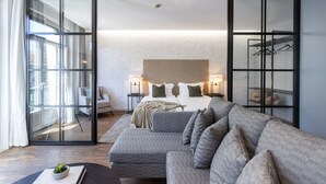 Un dormitorio moderno con una cama grande, un sofá gris y un ventanal que da a un balcón.