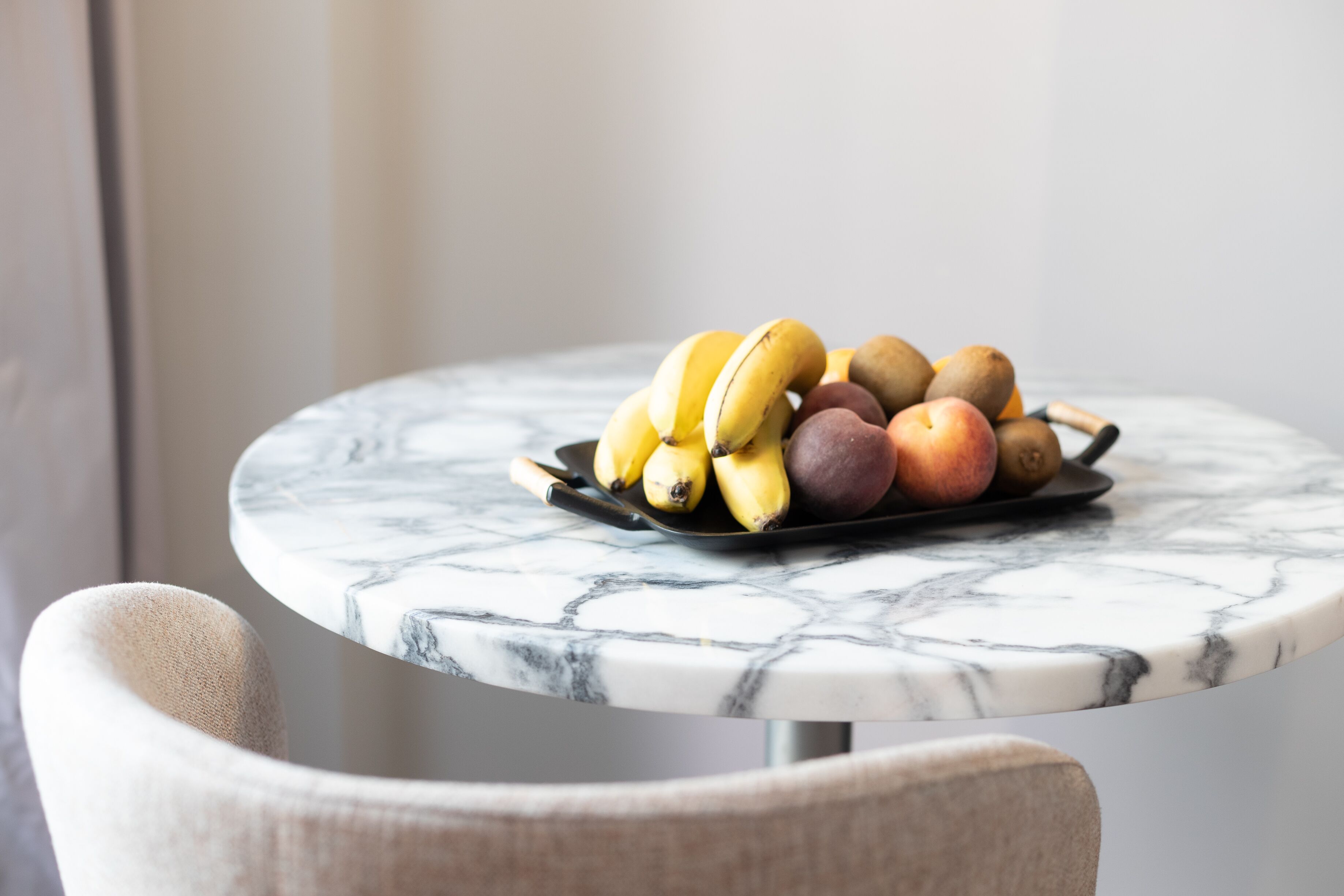 Une table en marbre sur laquelle se trouve un plateau de fruits contenant des bananes, des pommes et des kiwis.