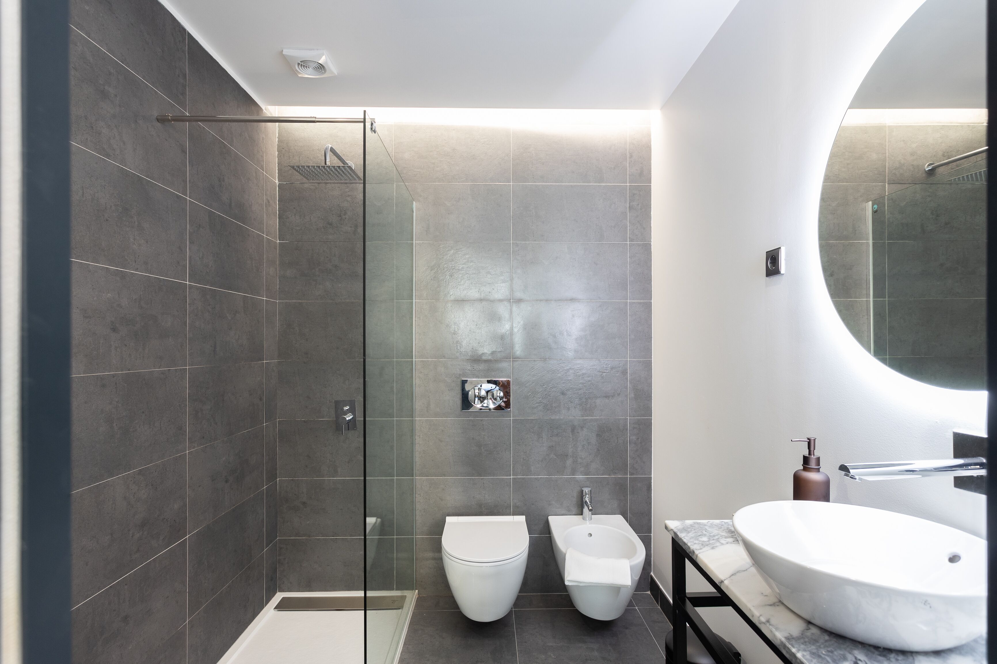 Une salle de bain moderne avec une douche à parois de verre, des toilettes blanches, un bidet et un grand lavabo ovale.