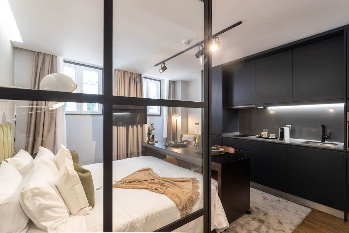 Quarto de hotel moderno com cama, mesa de cabeceira e uma kitchenette.