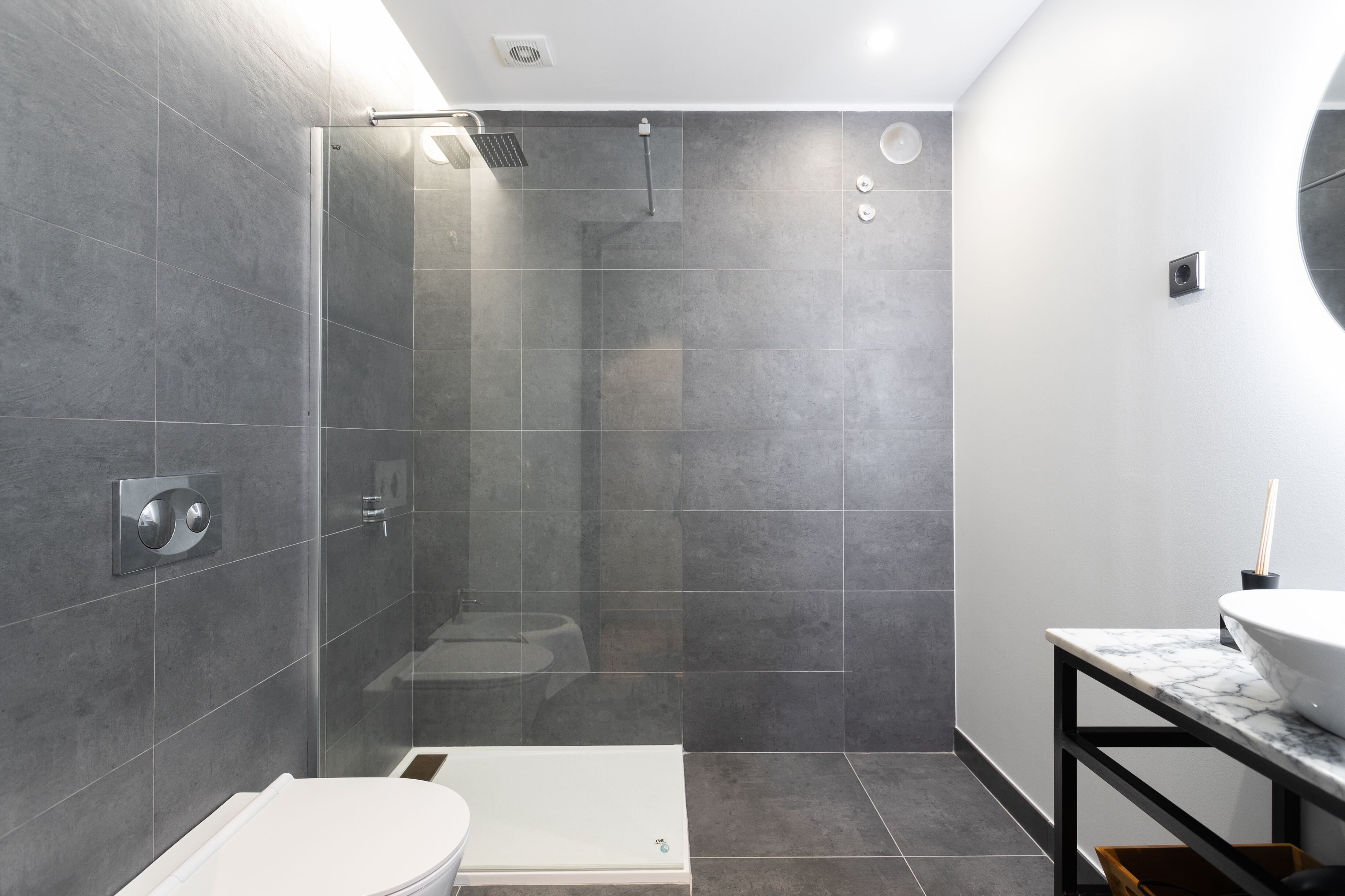 Un baño moderno con ducha de vidrio, inodoro blanco y encimera de mármol con lavamanos.