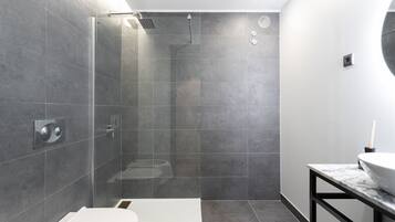 Un baño moderno con ducha de vidrio, inodoro blanco y encimera de mármol con lavamanos.