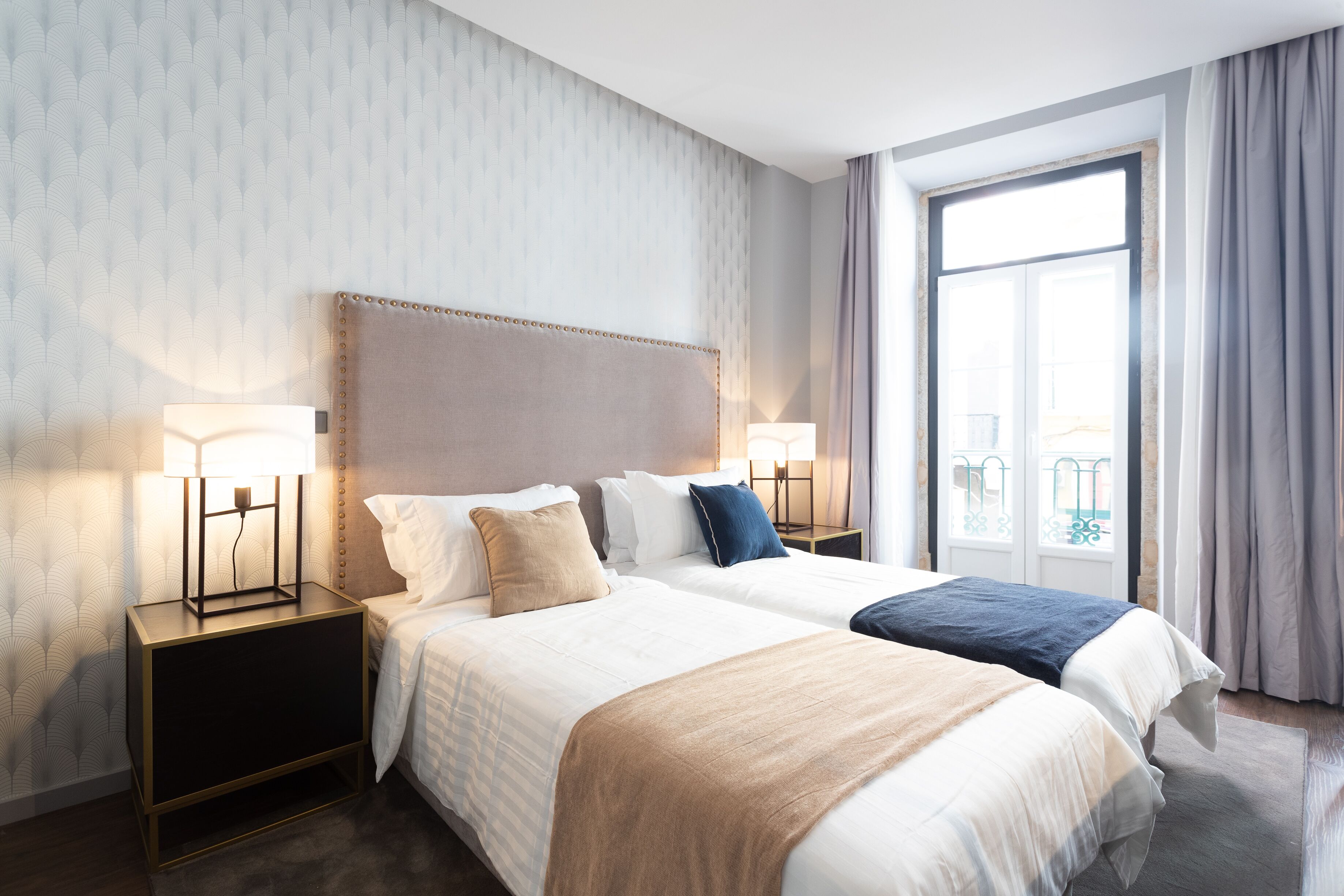 Et hotelværelse med to senge, et stort vindue og et natbord med en lampe.