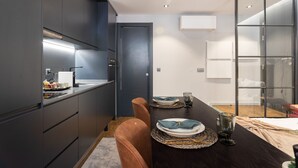 Una cocina moderna con armarios oscuros, una mesa de comedor dispuesta con platos y vasos, y una puerta que da a otra habitación.
