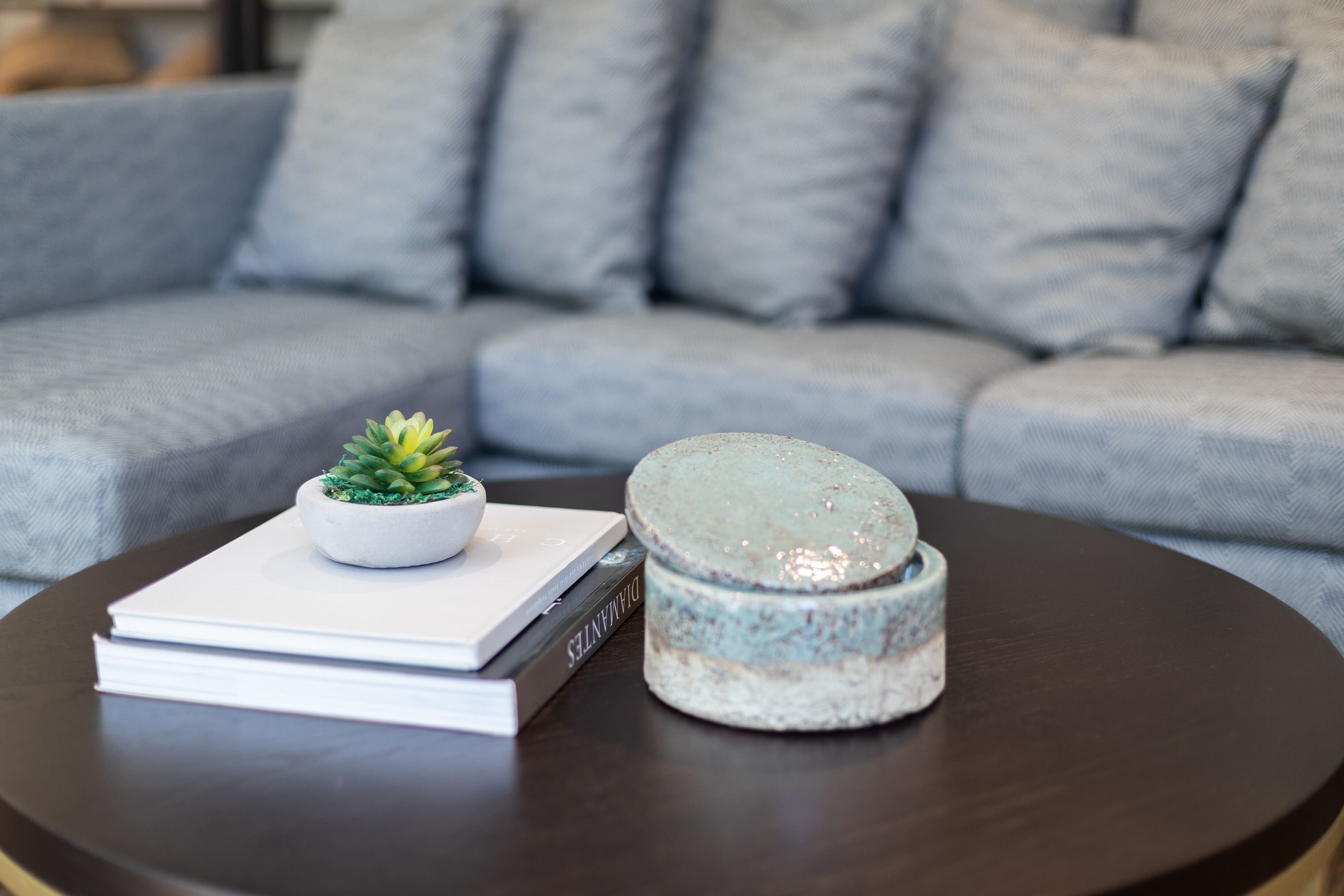 A round table with a book, a small potted plant, and a ceramic container.