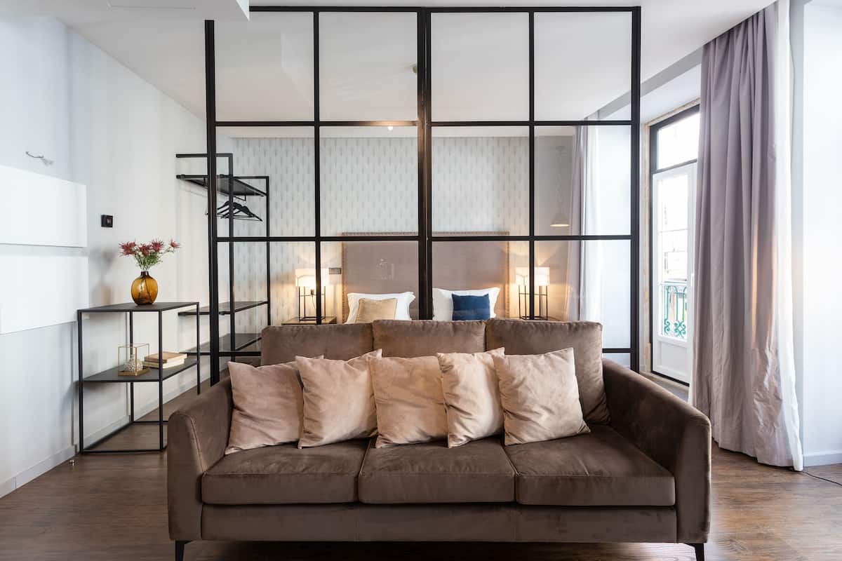 Uma sala de estar moderna com um sofá marrom, uma mesa de centro de vidro e uma estante de metal preta.