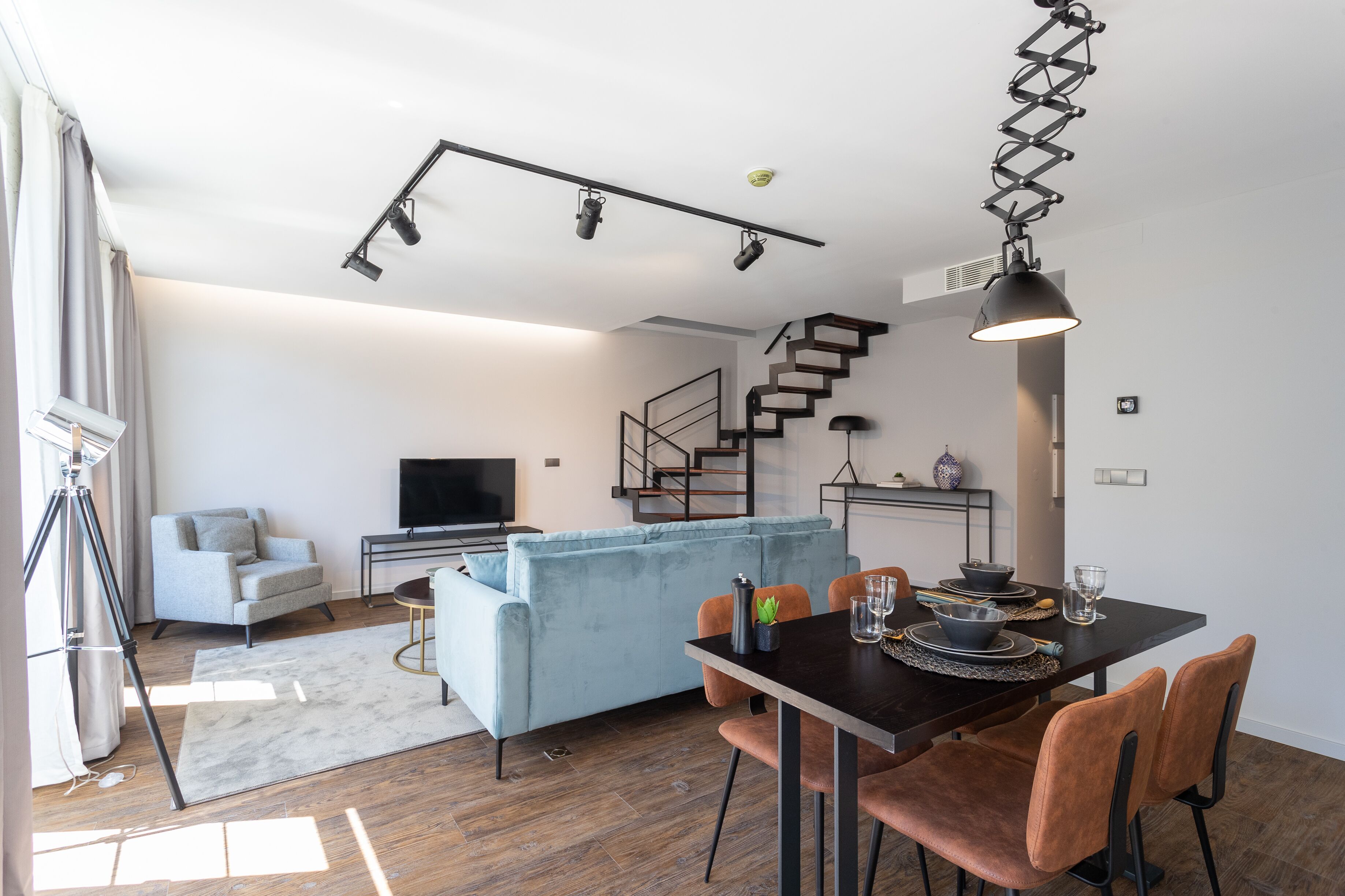 A modern living room with a sofa, TV, and dining area with chairs and a table.