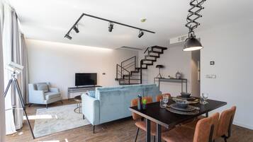 A modern living room with a sofa, TV, and dining area with chairs and a table.
