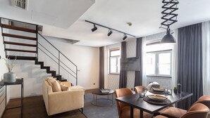 Una sala de estar moderna con sofá, mesa de centro y comedor con sillas. Una escalera conduce a un nivel superior.