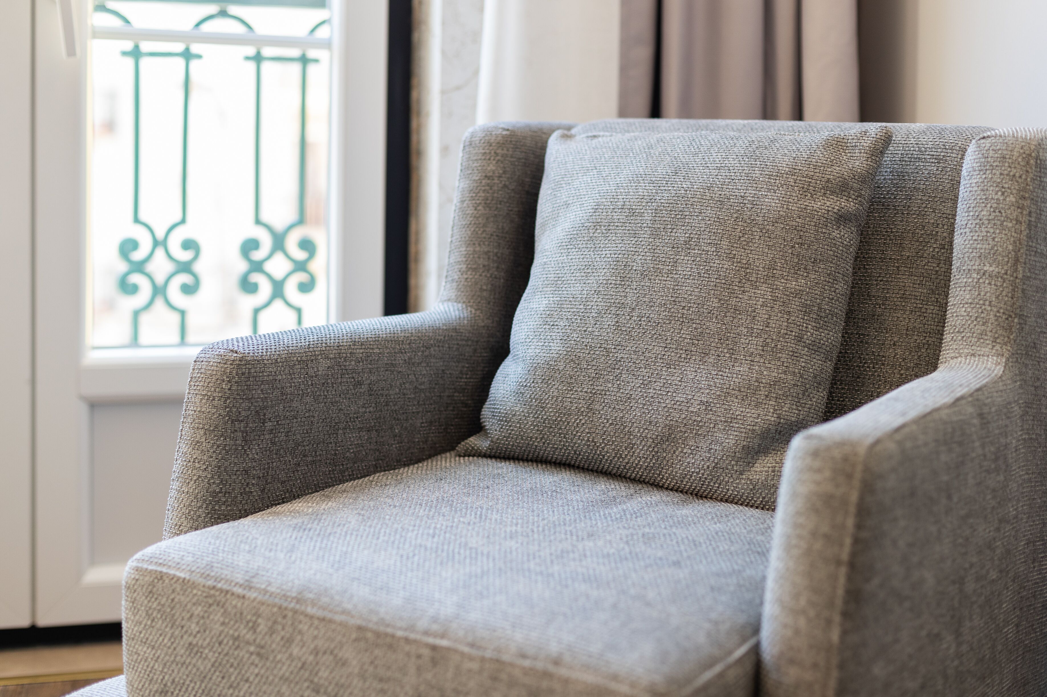 A grey armchair with a textured fabric, positioned near a window with a metal railing.