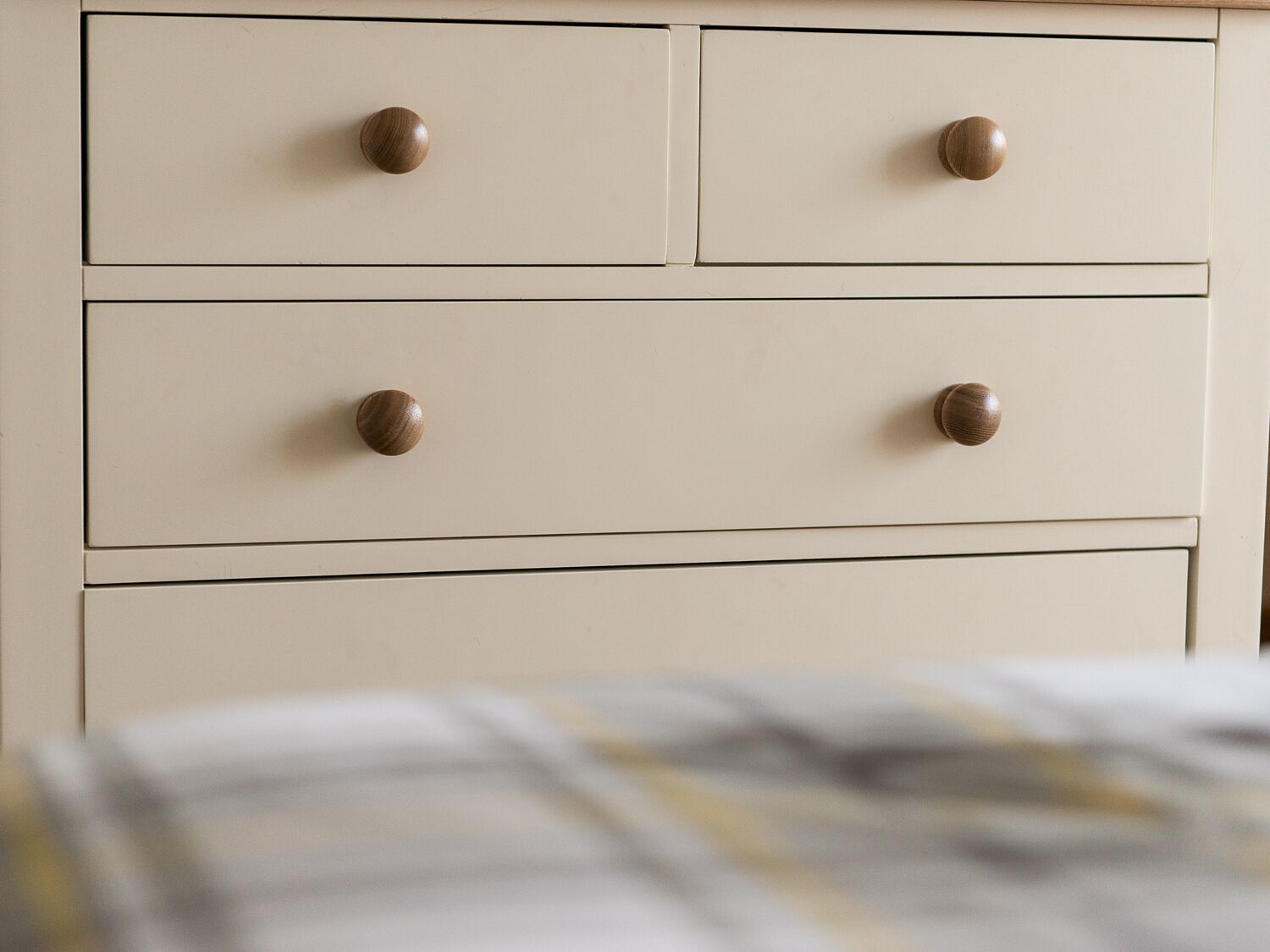 Una cassettiera beige con quattro cassetti, ognuno dotato di una maniglia in legno rotonda.