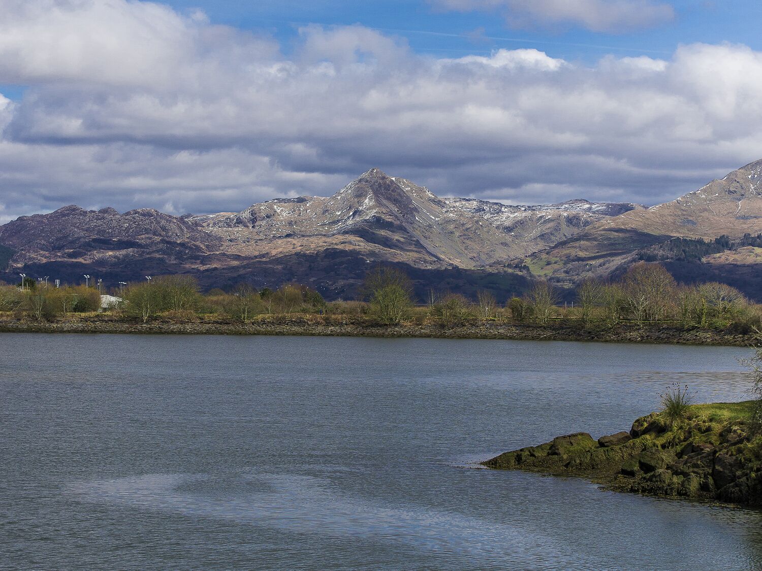 A lake with mountains in the background and a rocky shoreline.