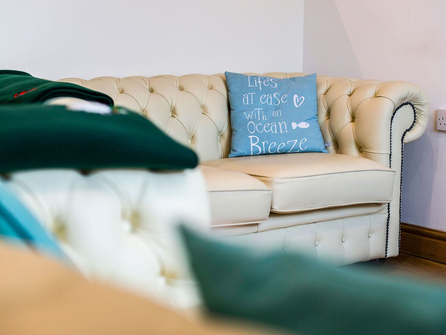 A tufted beige sofa with a decorative pillow that reads "LifE's AT ease With an Ocean Breeze".