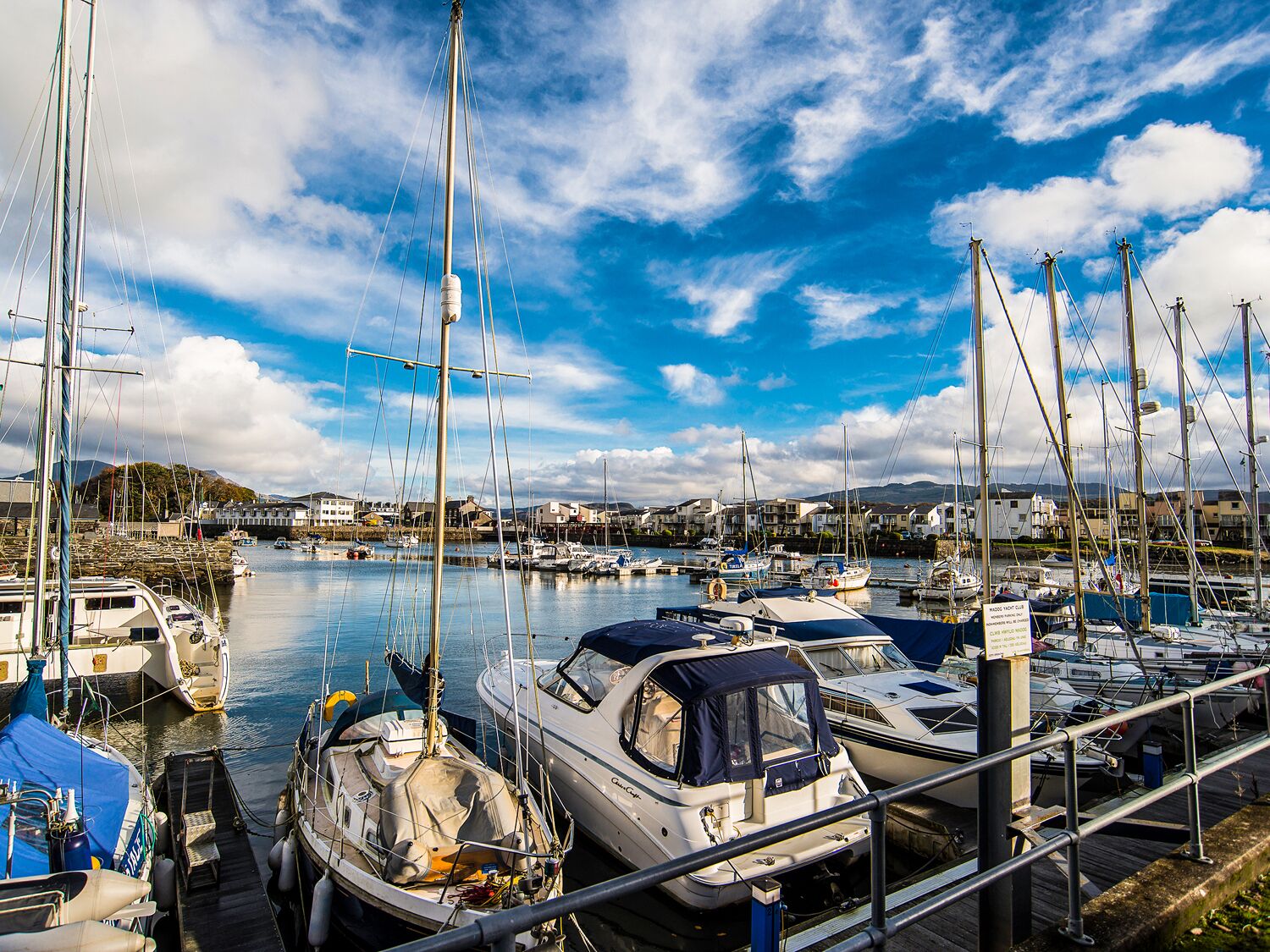 Un port de plaisance où sont amarrés de nombreux bateaux, une passerelle en bois et un ciel dégagé.