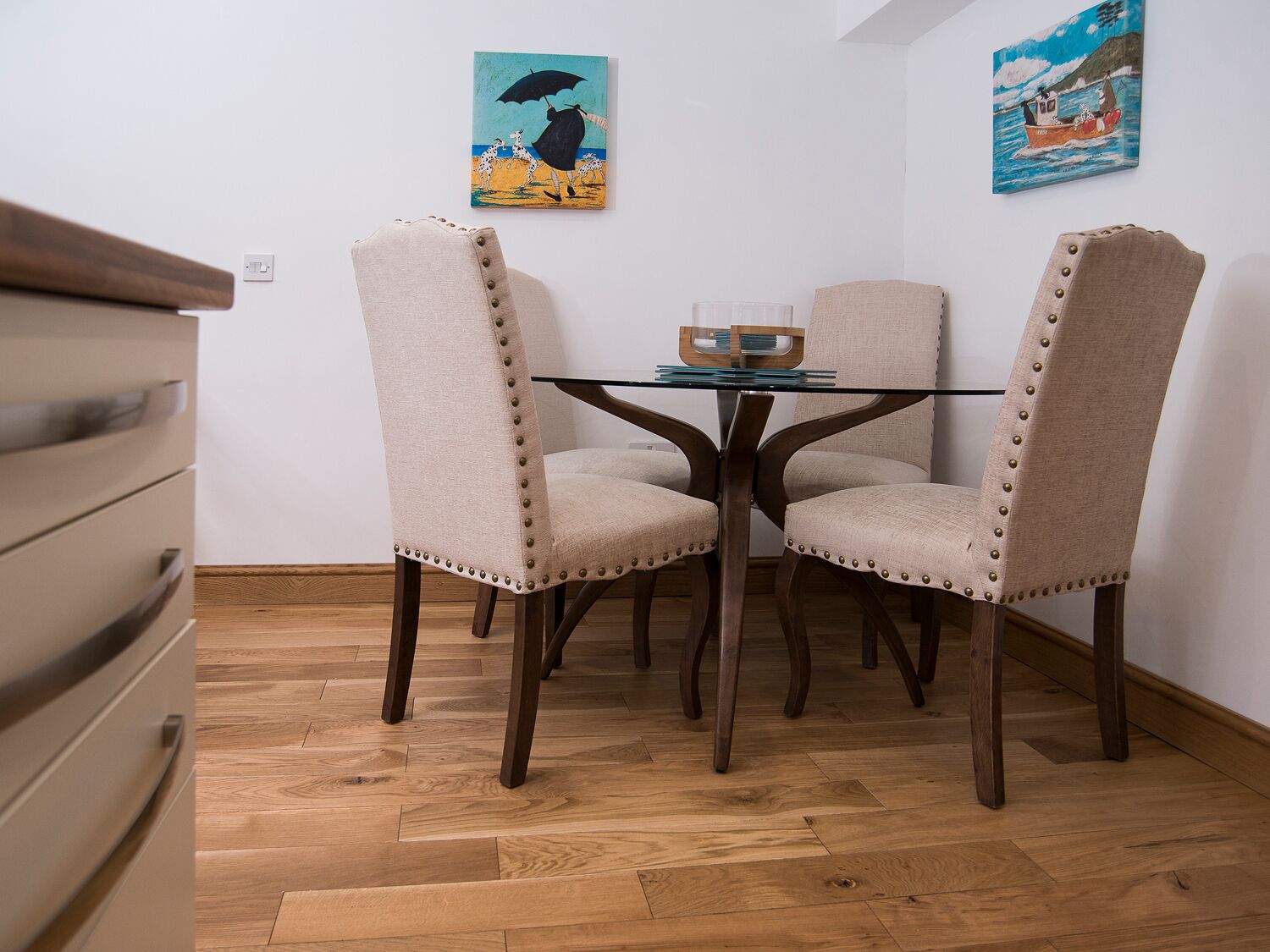 Comedor con mesa de vidrio rodeada por cuatro sillas tapizadas con tachuelas de metal.