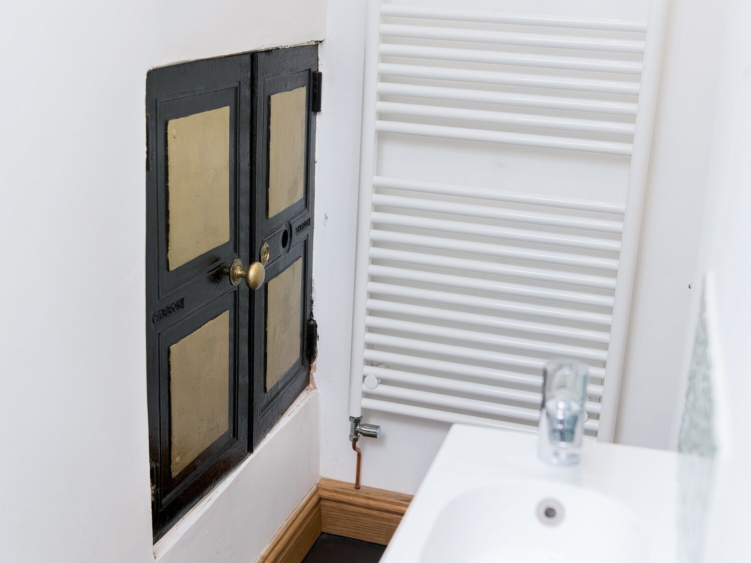 Een badkamer met een wit wastafel, een zwarte deur met glaspanelen en een witte radiator.
