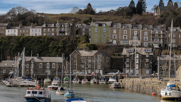 A harbor with boats docked, surrounded by stone buildings and a hillside in the background. - The Captain's Bank (Porthmadog)