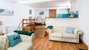A modern living room with a sofa, a chair, a dining table with chairs, and a kitchen area with a countertop and cabinets. - The Captain's Bank (Porthmadog)
