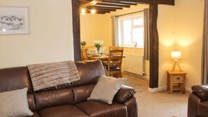 A cozy living room with a brown leather sofa, a wooden coffee table, and a dining area with a wooden table and chairs. - Caesamson (Caersws)