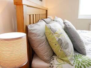 Un lit avec une tête de lit en bois, plusieurs oreillers et une lampe à rayures.