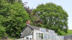 A two-story house with a stone facade, large windows, and a wooden fence. - Caesamson (Caersws)