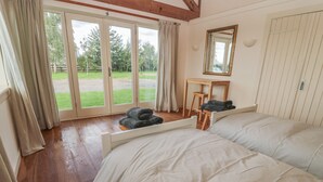 Une chambre avec deux lits, un bureau en bois, un miroir et une porte-fenêtre coulissante donnant sur un jardin.