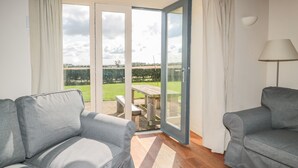 Une pièce avec deux canapés gris, un plancher en bois et une grande porte-fenêtre coulissante donnant sur un espace extérieur aménagé avec une table et des chaises.
