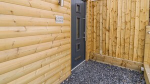 A wooden cabin with a dark door, a wooden fence, and a sign that reads "Cilan Lodge". - Cilan Lodge (Corwen)
